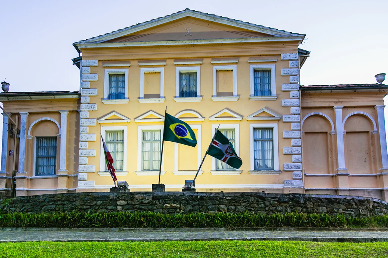 Fachada do Museu Municipal de São Bento do Sul, prédio histórico amarelo com bandeiras do Brasil, de Santa Catarina e da cidade
